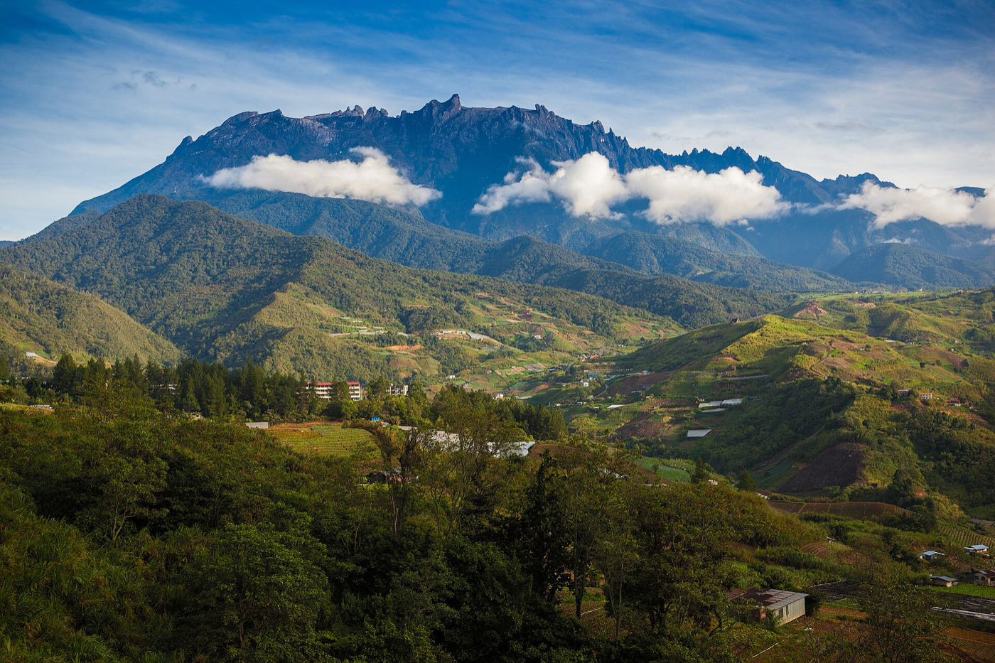 Jagged granite summit of Mount Kinabalu above green hills and farmland in Sabah